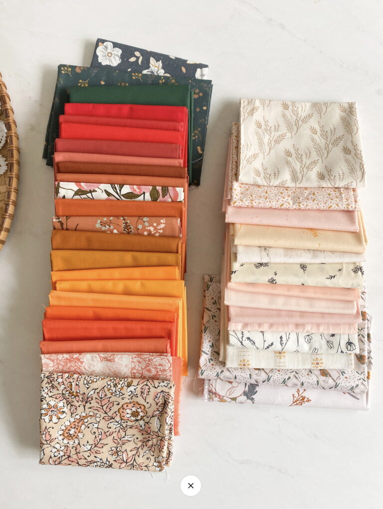 Two stacks of folded quilting fabrics for the Front Porch Quilt Along 2025. The left stack features vibrant warm tones like deep green, red, orange, and mustard, along with floral and botanical prints. The right stack contains soft low-volume fabrics in cream, blush, and ivory with delicate floral and nature-inspired designs.